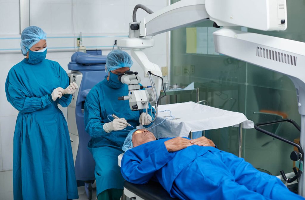 Ophthalmologist performing eye surgery with assistance, patient lying on operating table, medical equipment in background, emphasizing collaboration in advanced eye care.