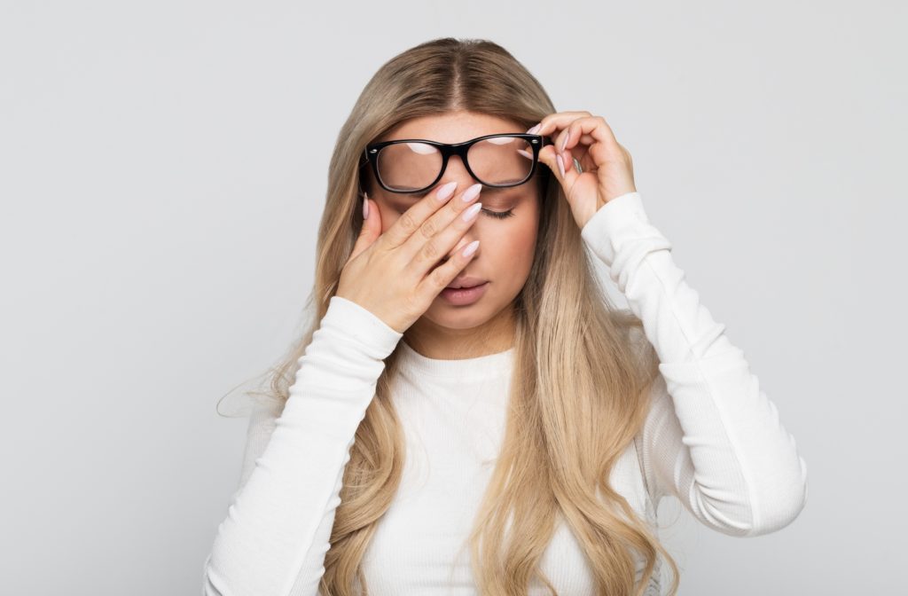 Woman experiencing discomfort while adjusting her glasses, illustrating headaches associated with new eyewear.