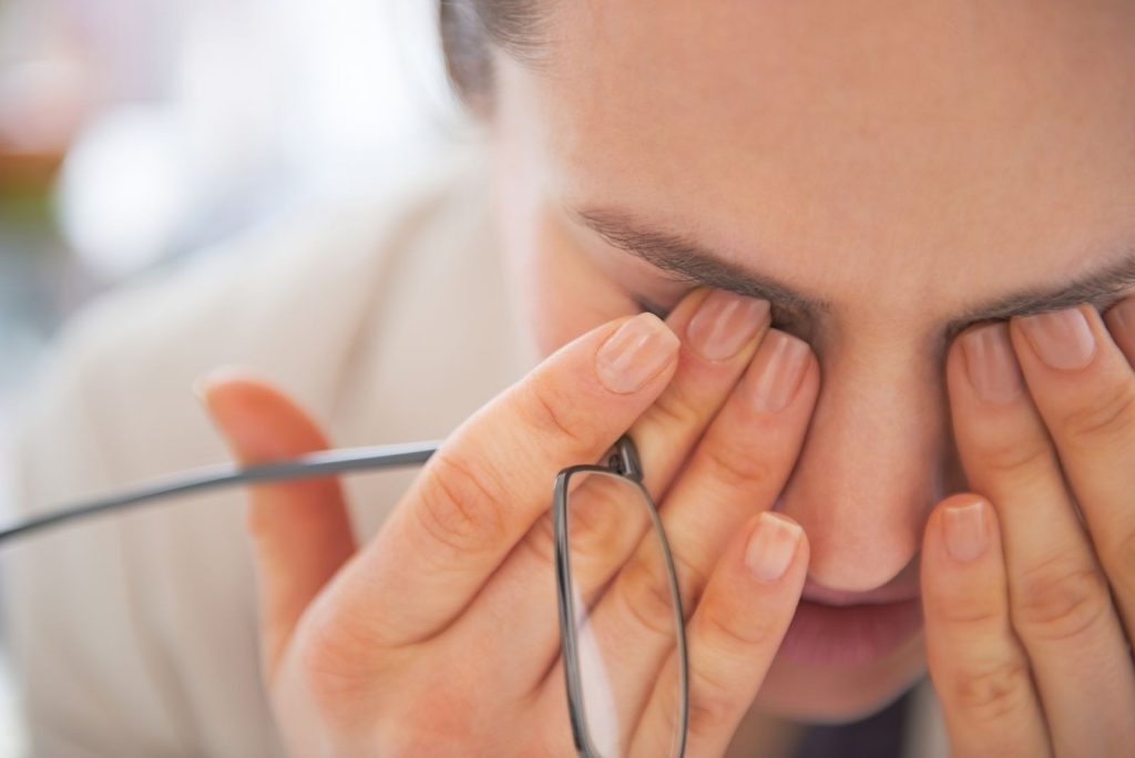 Woman rubbing her eyes while holding eyeglasses, illustrating signs of eye discomfort and fatigue related to common eye problems.